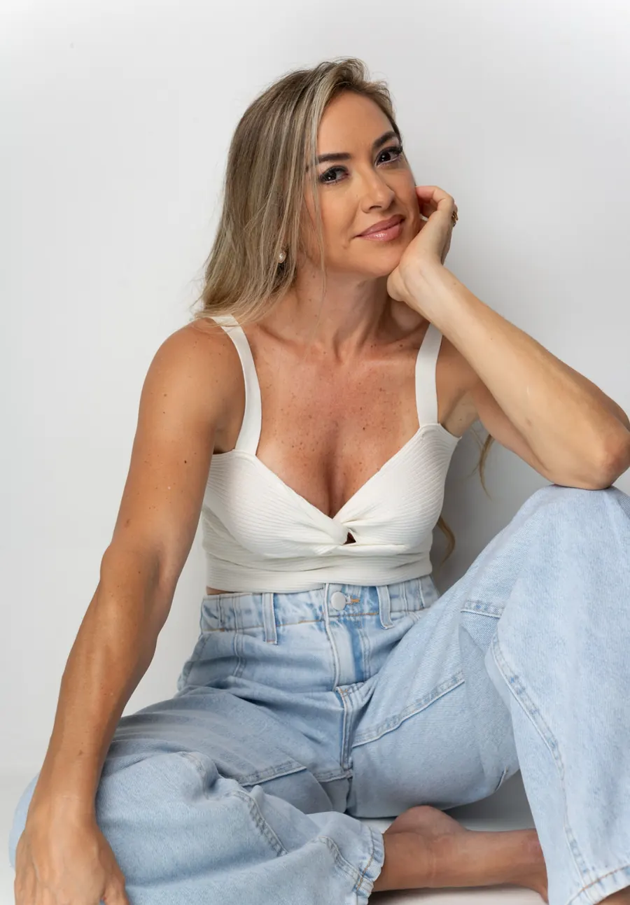 Tati sentada de forma descontraída, em fundo claro