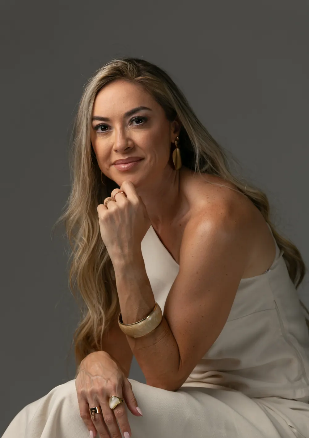 Retrato de Tati sorrindo, apoiada na mão, em fundo escuro